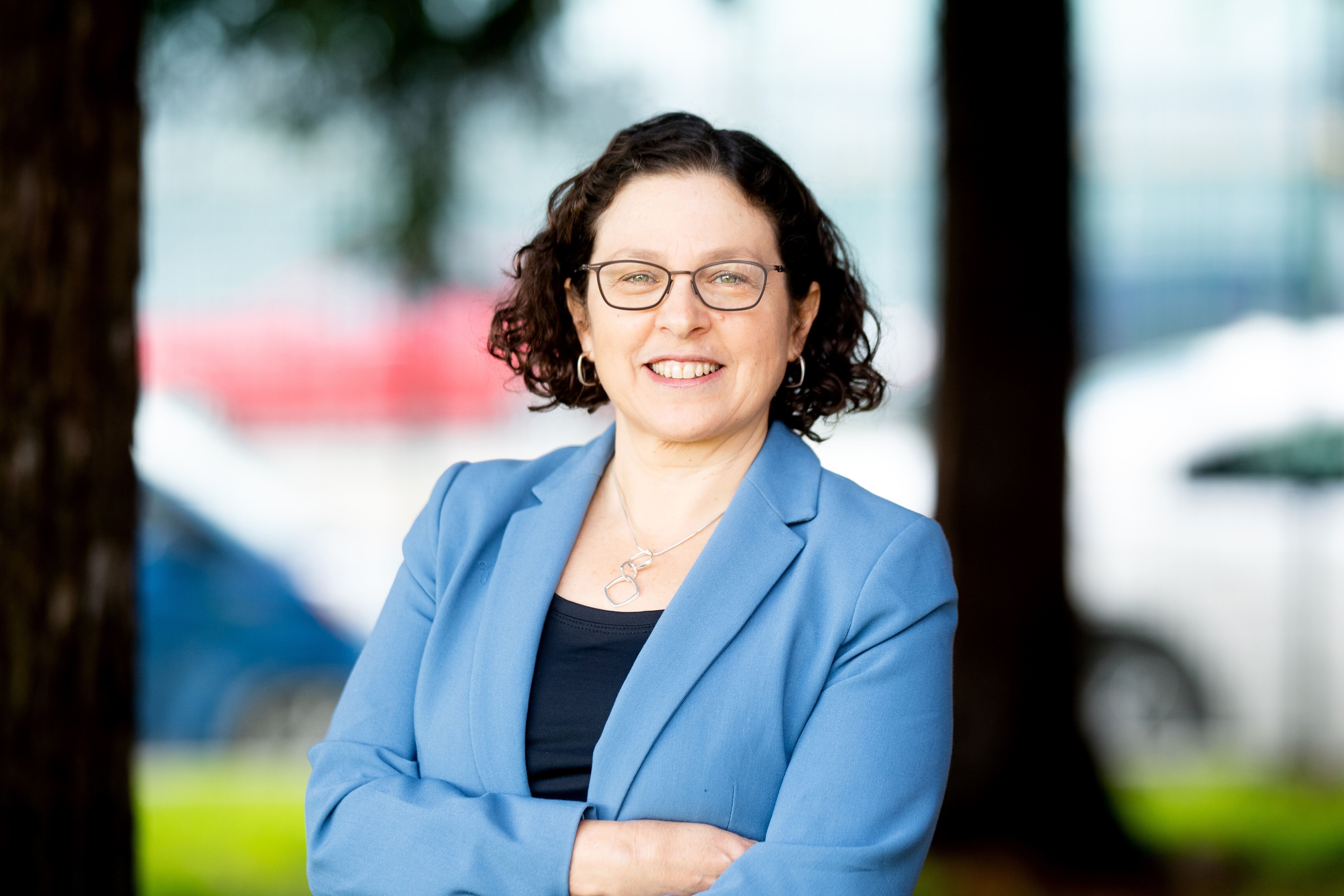 Photo of Margot Kushel smiling and crossing her arms. She is wearing a blue blazer.
